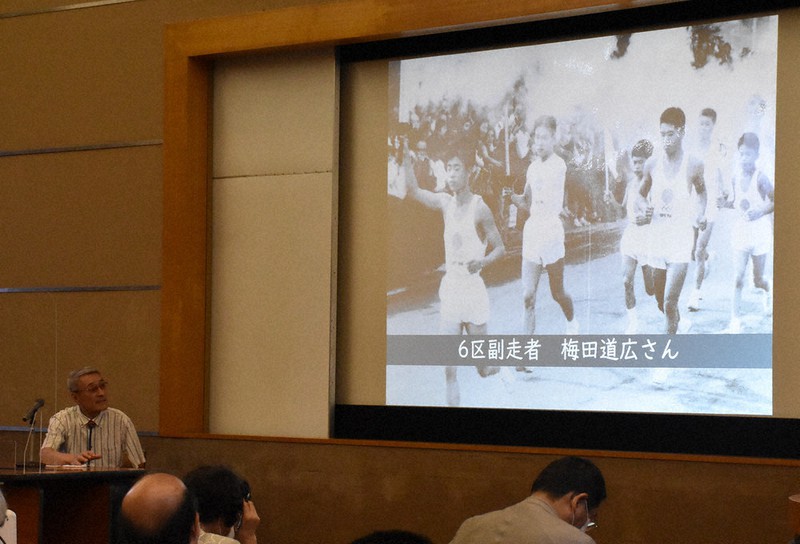 1964年の聖火リレーの写真が映し出された会場で当時を振り返る梅田道広さん(左)。57年前の写真の左から2人目が梅田さん=大津市御陵町の市歴史博物館で、菅健吾撮影