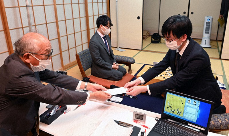 第76期本因坊決定戦七番勝負第3局で封じ手を立会の坂口隆三九段に渡す芝野虎丸王座(右)。中央奥は本因坊文裕=大阪府守口市で2021年6月1日、望月亮一撮影