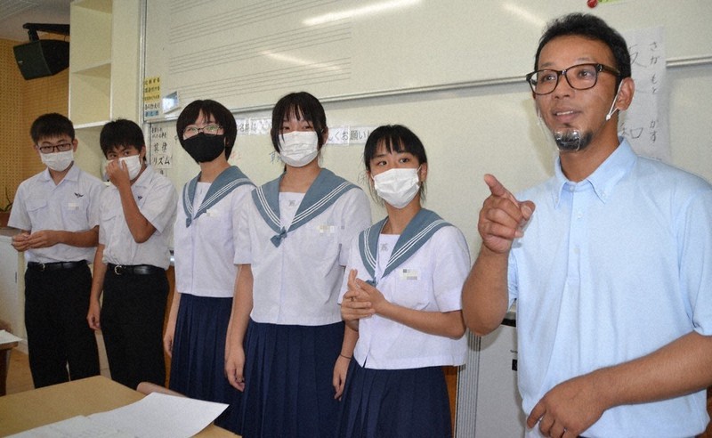 唐津市立肥前中音楽室で2年生に「私の名前は~」と自己紹介の手話を紹介する坂本さん(右)(画像)の一部を加工しています