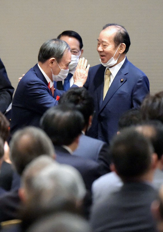 2020年の自民党二階派の政治資金パーティーで、あいさつのため手を挙げて登壇する菅義偉首相(左)を笑顔で迎える二階俊博幹事長=東京都千代田区で2020年10月7日午後4時45分、藤井太郎撮影
