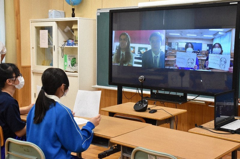 交流する英国の生徒ら(画面左側)に対し、自分たちで描いたイラストを使って好きな音楽について説明する本宮市立本宮第一中学校の生徒ら(左端、画面右側も同じ)=福島県本宮市で2021年6月8日午後3時46分、磯貝映奈撮影