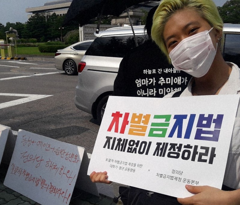 韓国の性的少数者による当事者団体に所属する女性。「差別禁止法 今すぐ制定せよ」と記したプラカードを手にしている=当事者団体「QUV」提供