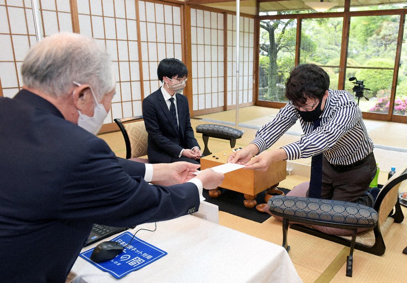 封じ手を立会の大竹英雄名誉碁聖(左)に手渡す本因坊文裕(右)。中央奥は挑戦者の芝野虎丸王座=北九州市で10日、上入来尚撮影