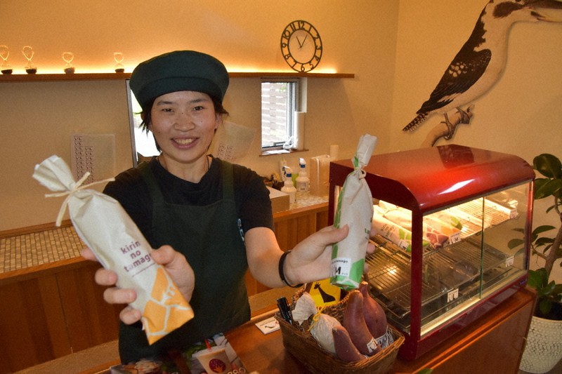 おしゃれなラッピングの冷やし焼きイモ「キリンのたまご」をPRする接客スタッフの村田夕夏さん=三重県伊勢市小木町の「クロフネファーム」で2021年6月11日午前11時6分、尾崎稔裕撮影