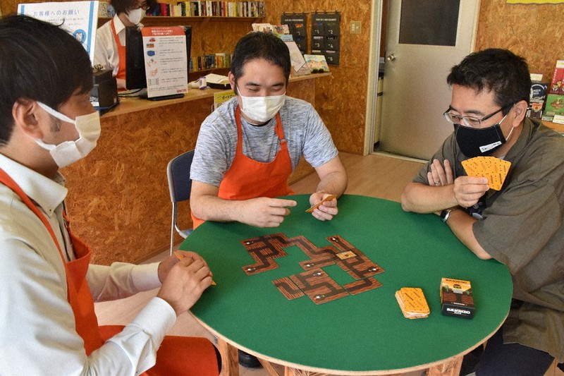 店員の説明を聞きながらカードゲームを試す客(右)=津市東丸之内の「SANTAS」で2021年6月19日、寺原多惠子撮影