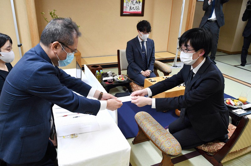第76期本因坊決定戦七番勝負第5局、封じ手を立会の山城宏九段(左)に手渡す挑戦者の芝野虎丸王座(右)。奥は本因坊文裕=長野県松本市の松本ホテル花月で2021年6月21日午後5時13分、丸山博撮影
