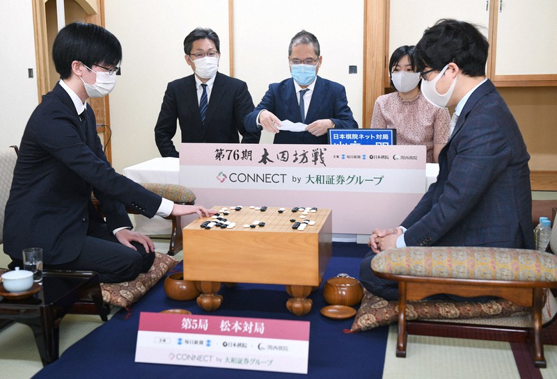 第76期本因坊決定戦七番勝負第5局、封じ手を打つ挑戦者の芝野虎丸王座(左)。右は本因坊文裕。奥中央は封じ手を開封する立会の山城宏九段=長野県松本市の松本ホテル花月で2021年6月22日午前9時4分、丸山博撮影