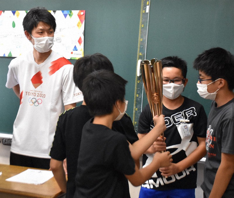 聖火ランナーのTシャツを着て、トーチを児童に見せる香月諒来さん(左)=宮城県名取市で