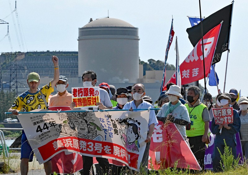 関西電力美浜原発3号機(奥)の再稼働に反対してデモ行進をする市民団体のメンバーら=福井県美浜町で2021年6月23日午後3時19分、山田尚弘撮影