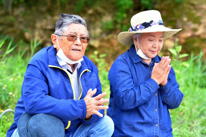 親代わりだった伯父の玉城亀さん、カミさん夫婦を追悼し、手を合わせて思いをはせる玉城清輝さん。右は妻の千代子さん=沖縄県糸満市で2021年6月23日午後3時8分、平川義之撮影