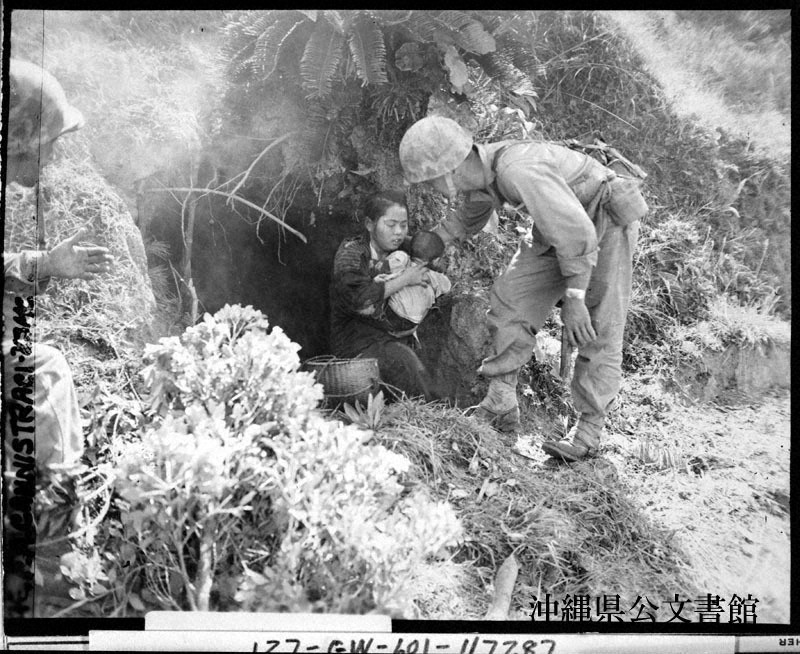 米兵に見つかり、赤ん坊を抱いてガマから出る住民=1945年4月、沖縄県公文書館提供