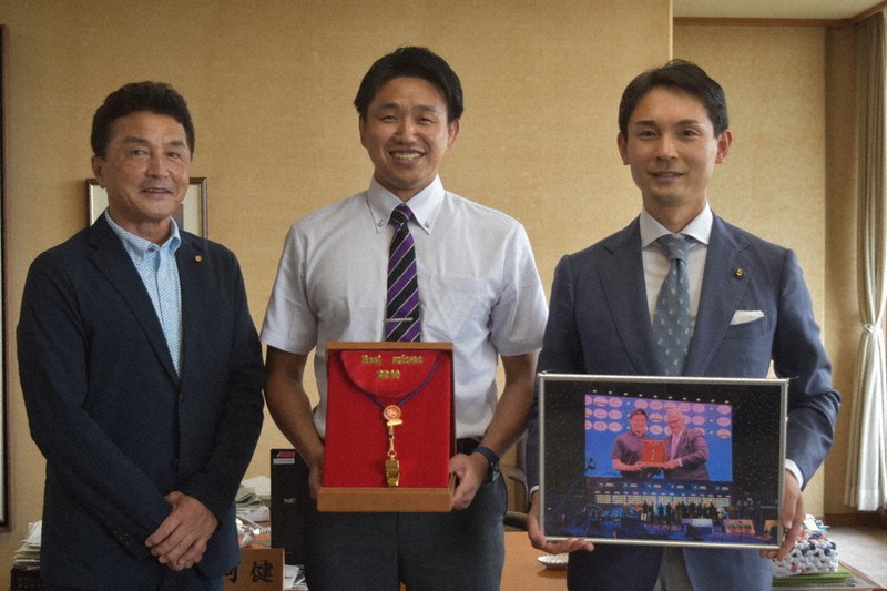 東京五輪でレスリング競技の審判員に選ばれた小池邦徳さん(中央)。手にするのは「ゴールデンホイッスル賞」で授与された金のホイッスル=奈良県天理市で、広瀬晃子撮影