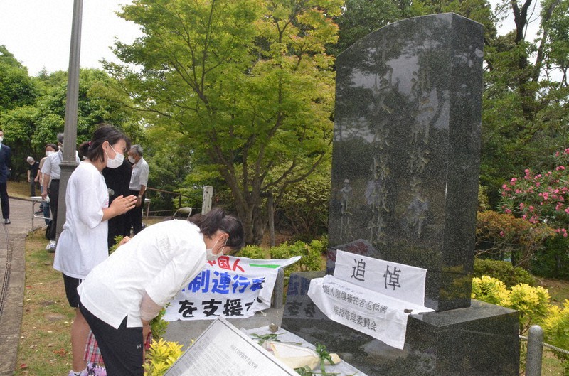 追悼碑の前で献花し手を合わせる参列者