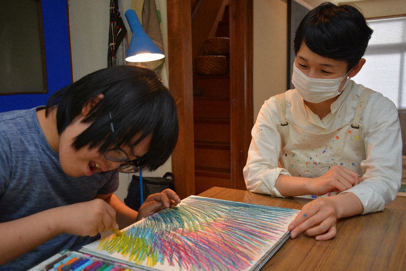 画用紙にクレヨンで色を塗る岩藤桜時さん(左)と、見守る栗山千尋さん=島根県浜田市の「アトリエ・スノイロ」で、萱原健一撮影