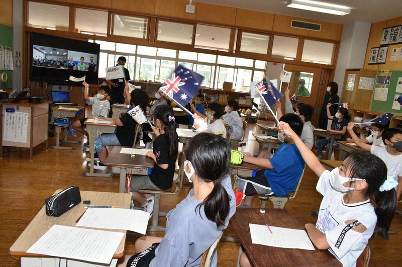 東京五輪豪州トランポリン代表とのオンライン交流会で、旗を振って選手を応援する児童たち=茨城県稲敷市高田の市立高田小学校で2021年7月14日、庭木茂視撮影