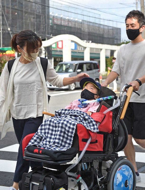 人工呼吸器と胃ろうをつけ、両親とともにバギーで小学校に向かう佐野涼将さん(中央)=相模原市中央区で2021年7月、前田梨里子撮影