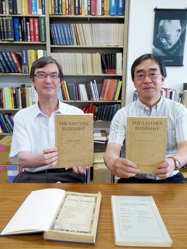 刷新した東方仏教徒協会の英文学術誌を手にする大谷大のローズ名誉教授(左)と井上教授。手前左は100年前の創刊号=京都市北区で2021年7月16日午後4時42分、千葉紀和撮影