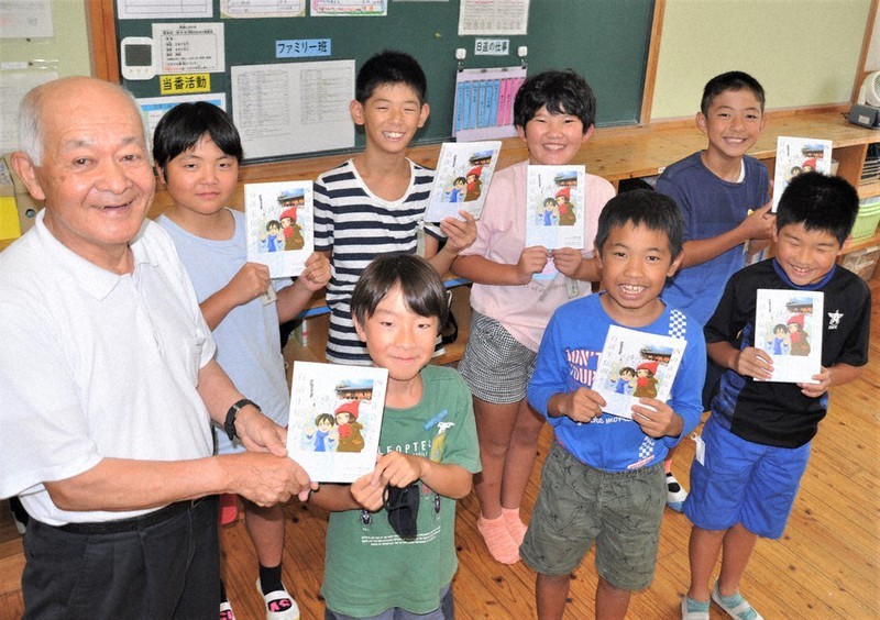 原作者の原田さん(左)と贈られた漫画を手にする児童ら