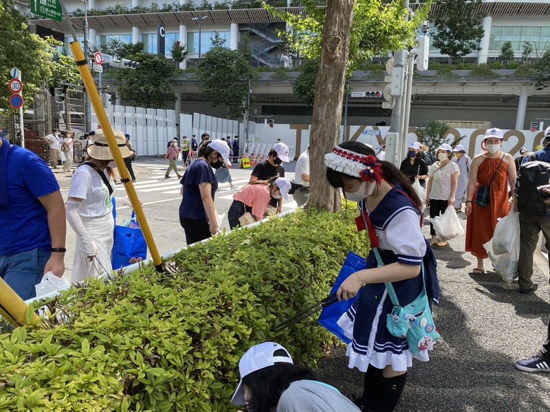 ゴミ拾いをする参加者。後ろに見えるのは国立競技場=東京都渋谷区で2021年7月23日午前8時50分、松倉佑輔撮影