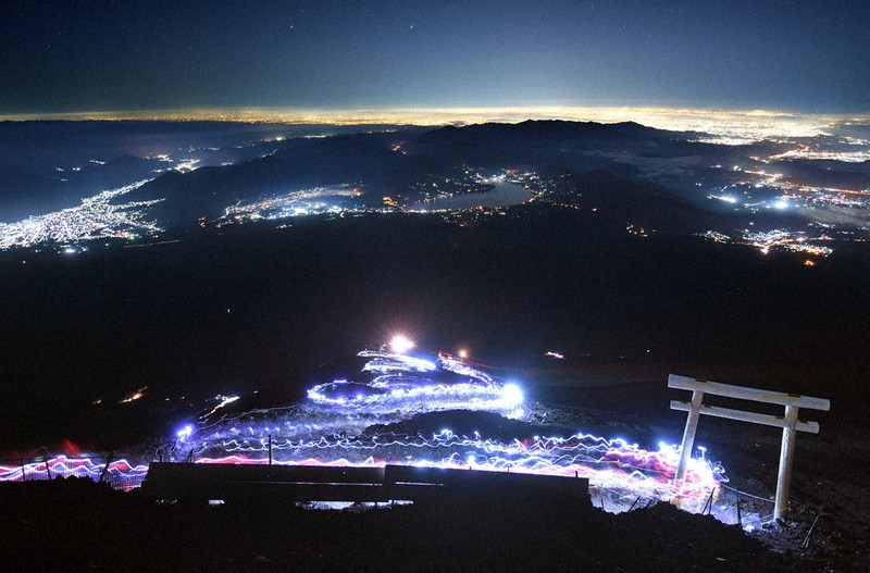 梅雨明けの発表直後の日曜未明。富士山頂を目指す登山者のヘッドランプが、2年ぶりとなる光の波を描いた。中央奥は山中湖=山梨県側の富士山吉田口9合目で2021年7月18日午前2時29分、手塚耕一郎撮影(64秒露光)
