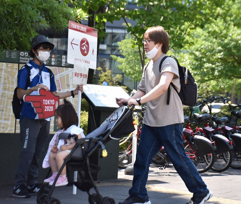 JR仙台駅東口でスタジアム行きのシャトルバス乗り場へ誘導する立て看板を持つ都市ボランティアの男性(左)=仙台市宮城野区で2021年7月24日午後1時半、滝沢一誠撮影
