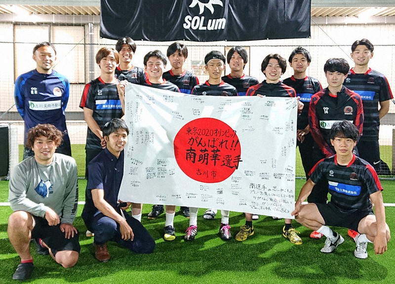 寄せ書きの日の丸を手に南選手を応援するフットサルチーム「ディセンドーラ吉川」。前列右端が同級生の塩崎巧巳さん=埼玉県吉川市で2021年6月30日(同市提供)