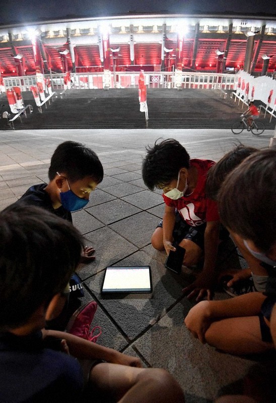 日産スタジアム(奥)まで訪れ、会場内で行われているサッカー男子の日本-フランス戦のライブ中継を見る子どもたち=横浜市港北区で2021年7月28日午後8時41分、平川義之撮影