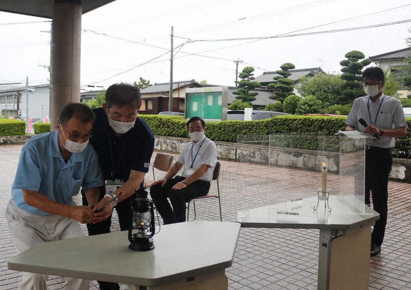 和ろうそくからランタンへと灯を移す市身体障がい者福祉協会長の秋原さん(左)
