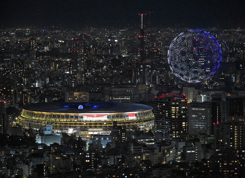 国立競技場そばの上空で、市松模様のエンブレムを描くドローンの編隊飛行(右上)=東京都渋谷区の渋谷スカイから7月23日、手塚耕一郎撮影