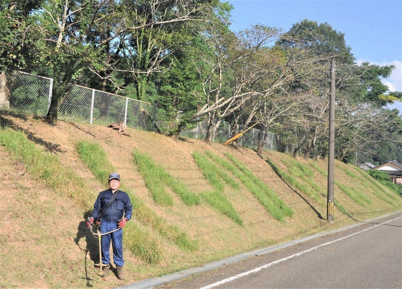 校庭下の土手に草で浮かび上がる笑顔の顔文字と黒木さん=宮崎県日向市の市立塩見小前で2021年8月25日午後4時27分、重春次男撮影