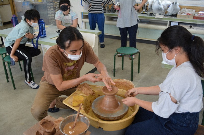 ろくろを使った器作りを女児へ教える垣野さん