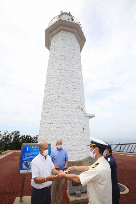 灯台前で田辺海上保安部の上野春一郎部長(右)から承認書や鍵を受け取る小薮清信理事長ら=和歌山県日高町阿尾で2021年8月26日、山本芳博撮影