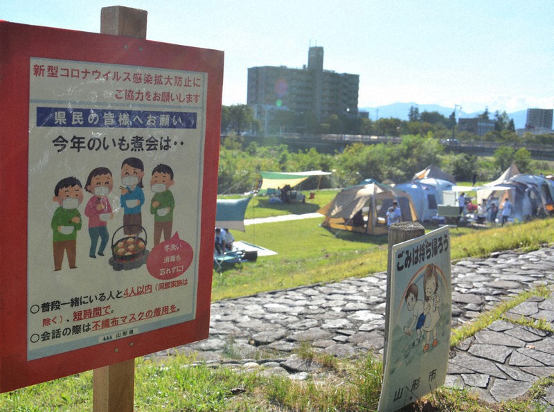 芋煮会の際の感染防止策を呼びかける看板。奥のテントでは、家族連れらが会を楽しんでいた=山形市で2021年9月19日、井川加菜美撮影