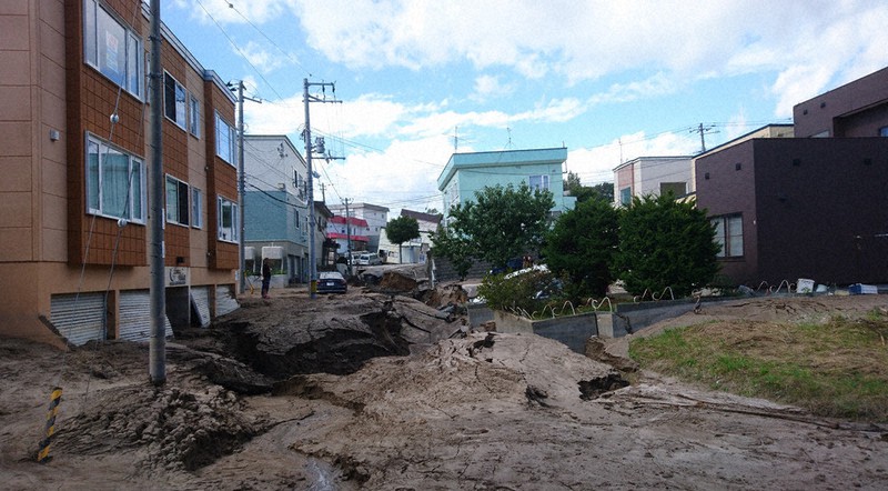 地震当日の住宅街。大量に流出した土砂が道路を覆い、奥の住宅は大きく傾いていた=札幌市清田区里塚地区で2018年9月6日午前9時28分、土谷純一撮影