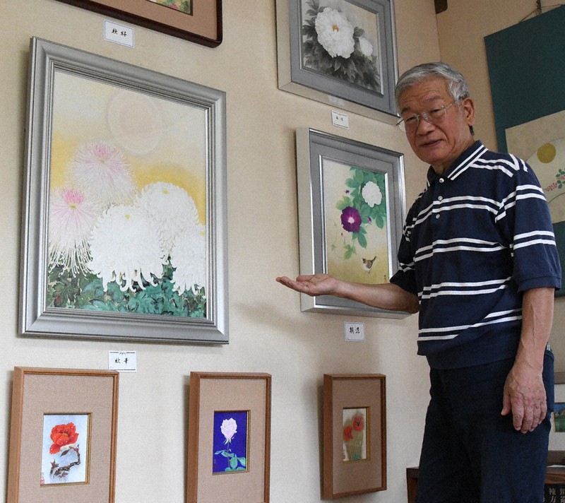 花を描いた作品を紹介する日本画家の大久保徹哉さん=松江市鹿島町北講武の「ぎゃらりー彩路」で、目野創撮影