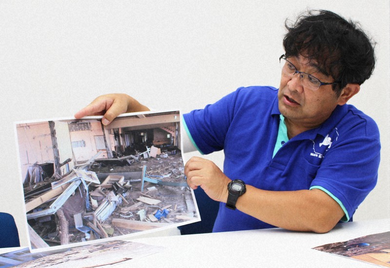 震災当時、請戸小の教務主任として避難を経験した佐藤信一教諭。手に持っているのは自衛隊が震災直後に撮影した校内の写真=福島県浪江町の町立なみえ創成小学校で2021年10月6日午後5時2分、尾崎修二撮影
