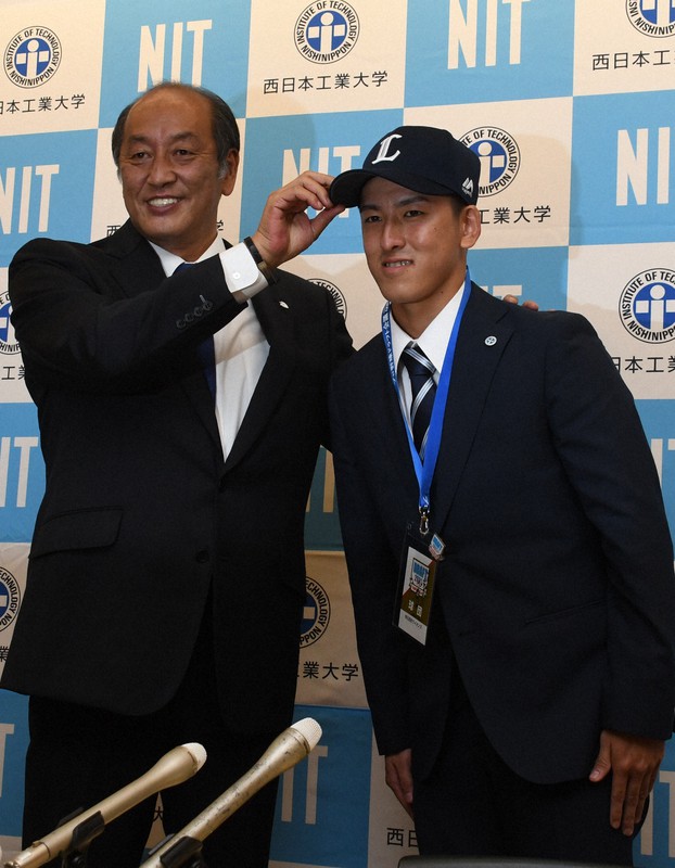 1位指名のあいさつを終え、隅田知一郎投手(右)に西武の帽子をかぶせる渡辺久信ゼネラルマネジャー=福岡県苅田町新津の西日本工大で2021年10月14日午前11時11分、松本昌樹撮影