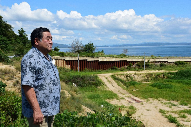 瀬戸内海に臨む不法投棄現場を見つめる住民の安岐正三さん。海の手前に見えるのが撤去予定の遮水壁=香川県土庄町・豊島で2021年9月6日午前10時19分、潟見雄大撮影