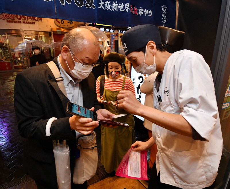新型コロナワクチン接種の証明書の写真をスマートフォンで見せて飲食店に入店する人たち=大阪市中央区の「串かつだるま 道頓堀店」で2021年10月25日午後5時47分、木葉健二撮影(画像の一部を加工しています)