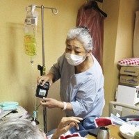 70代男性の自宅で、点滴の薬液を交換しなら容体を尋ねる露木理恵さん＝甲府市内で2021年10月22日、山本悟撮影