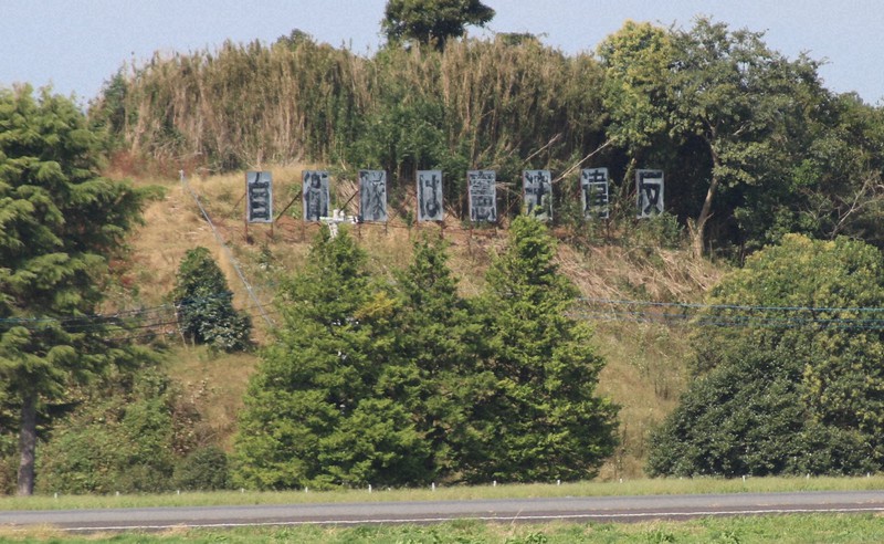 航空自衛隊百里基地の滑走路(手前)の奥の丘に立つ「自衛隊は憲法違反」の看板。設置から40年余りがたち、劣化が進んでいる=茨城県小美玉市で2021年10月11日、飼手勇介撮影