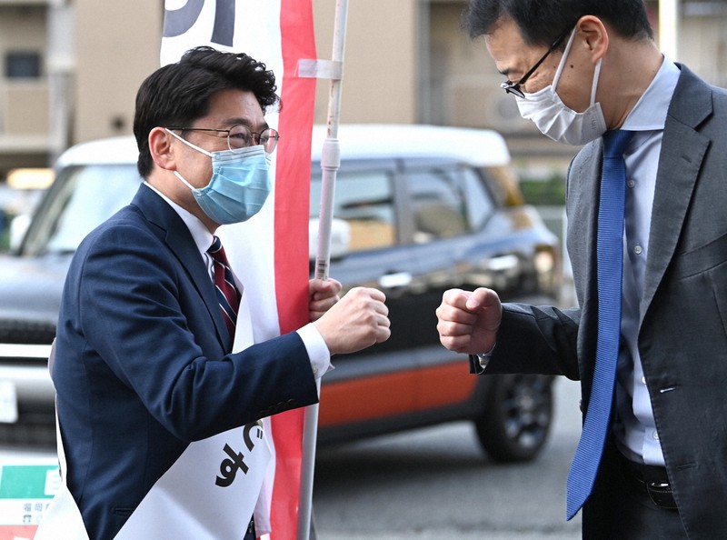 当選から一夜明け、交差点に立ち通勤する人とグータッチをかわす鬼木誠氏(左)=福岡市中央区で2021年11月1日午前7時52分、徳野仁子撮影