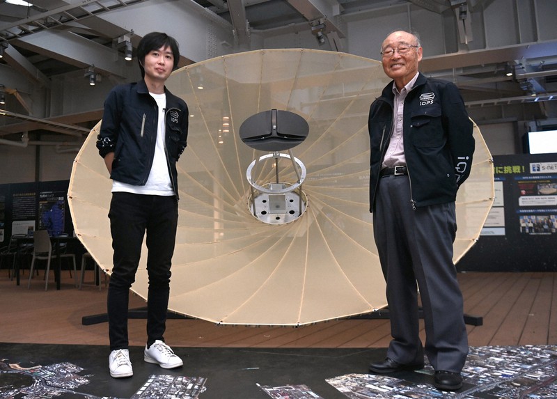 「人工衛星の開発を通じて八坂先生の知を受け継いでいきたい」と語る大西俊輔さん(左)と、「師匠」の八坂哲雄さん。後ろは人工衛星の実寸大実験機=福岡市博多区で2021年10月17日、徳野仁子撮影
