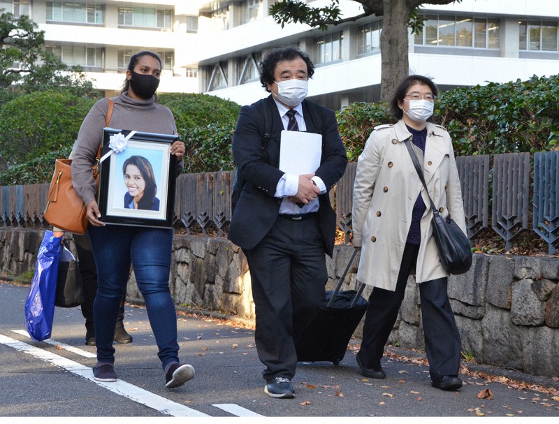 ウィシュマさんの遺影を手に告訴状の提出に向かう(左から)ポールニマさん、指宿昭一弁護士、駒井知会弁護士=名古屋市中区の名古屋地検が入る名古屋法務合同庁舎前で2021年11月9日午後3時45分、道永竜命撮影