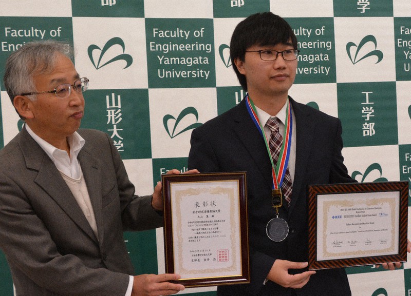 表彰状やメダルを披露する丸山さん(右)と近藤教授=山形県米沢市の山形大学工学部で2021年11月10日、佐藤良一撮影