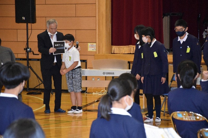 児童らに楽譜の大切さを理解させるための「伝言ゲーム」をする三枝さん(奥左)=甲府市の市立北新小で2021年11月30日、照山哲史撮影