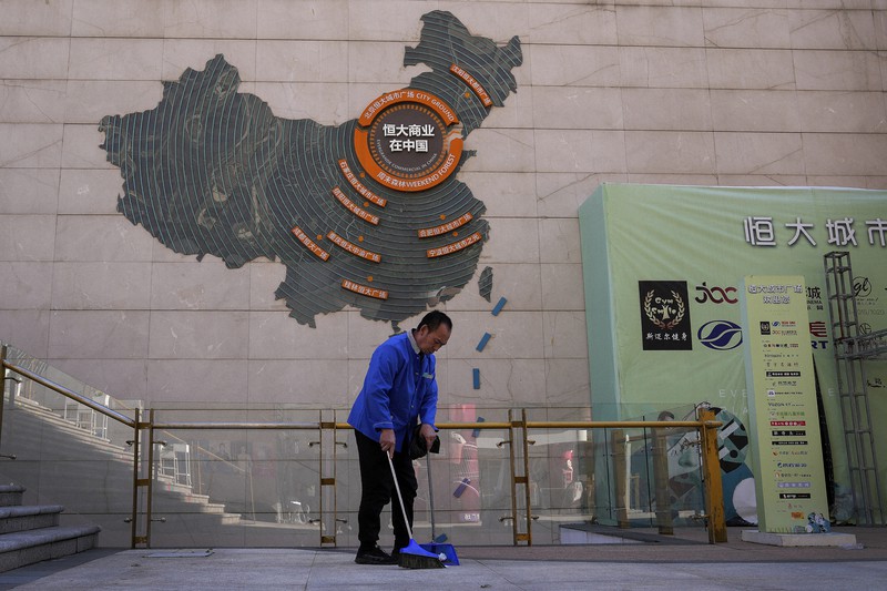 中国恒大集団の開発計画を示す地図の前を掃除する清掃員=北京で2021年9月21日、AP