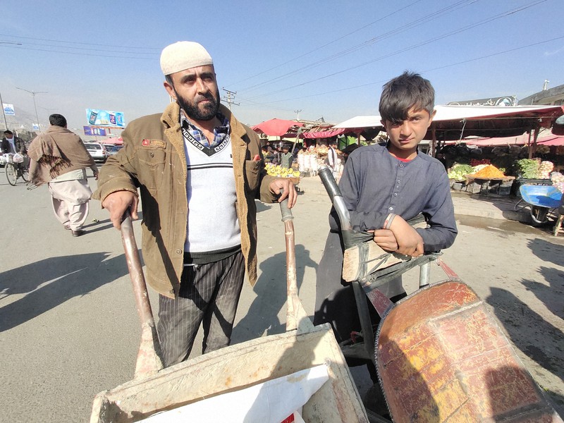 市場で買い物客から荷物運びの依頼が来るのを待つザビフラさん(左)=アフガニスタンの首都カブールで2021年12月4日、松井聡撮影