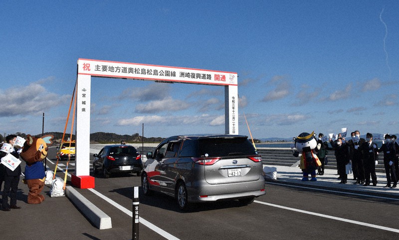 「洲崎復興道路」の開通式典後、車列パレードをする関係車両と、見送る人たち=宮城県東松島市野蒜洲崎で2021年12月23日午前10時40分、百武信幸撮影