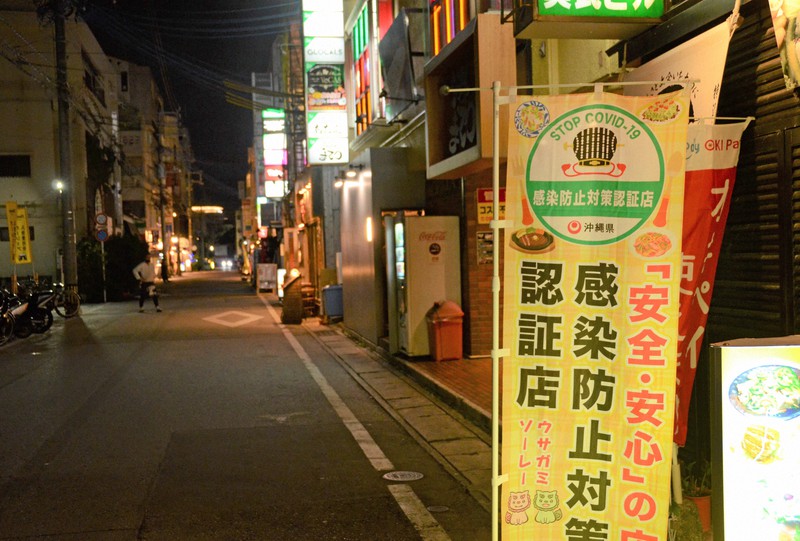 まん延防止等重点措置の適用が決まり人通りがまばらな繁華街。感染防止対策の認証を受けたことを示すのぼりが揺れていた=那覇市内で2022年1月7日午後7時4分、竹内望撮影